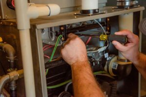 HVAC technician using diagnostic tool to inspect internal furnace wiring and components during maintenance service.