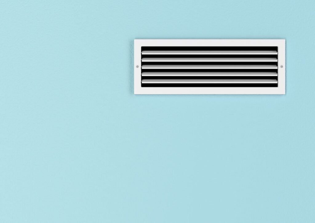 White rectangular air conditioning vent with black horizontal slats mounted on light blue wall.