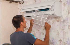 Technician installing a white mesh air filter into a wall-mounted split-system air conditioning unit for maintenance and purification.