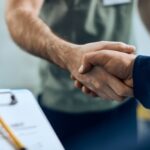 Two people shaking hands over a clipboard during a service agreement discussion.